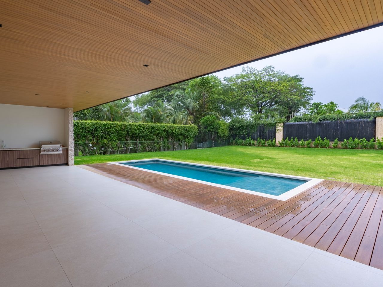 Terraza techada con cielo de madera sobre la piscina y el jardín